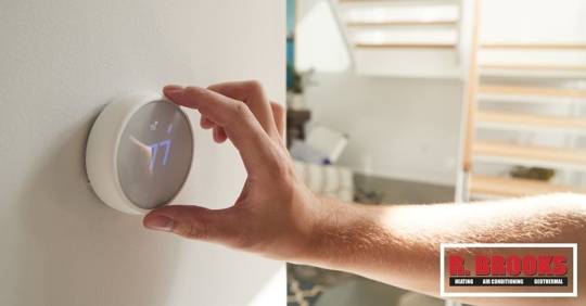 A hand holding a wall smart thermostat set to 77 degrees