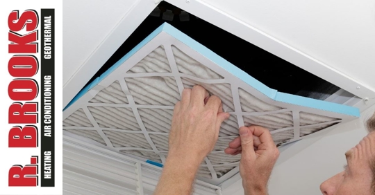 A man inserting a square air filter into a ceiling vent